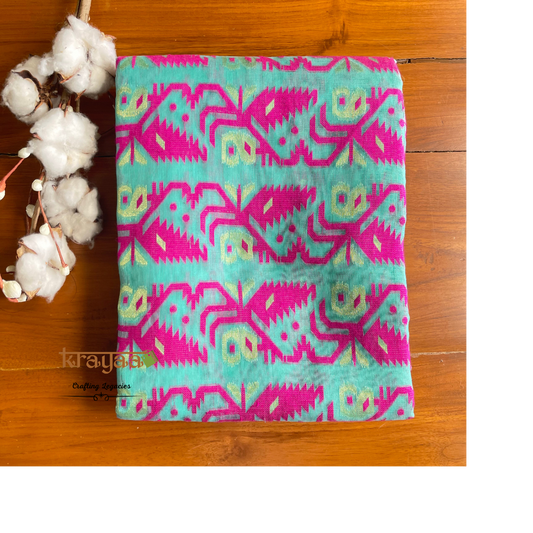 Turquoise fabric with pink and green geometric pattern on a wooden surface with cotton flowers.